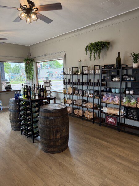 Wide view of the shop interior — whiskey-barrel display table in front of the cellar wall, with apparel racks and storefront window light
