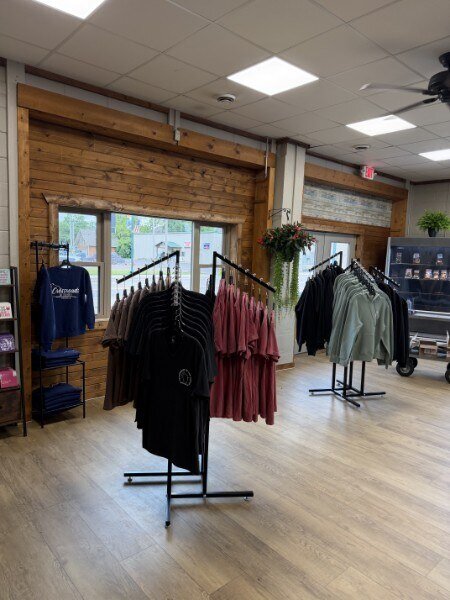 Branded apparel display — Crossroads of the North tees, hoodies, and crewnecks on rolling racks inside the shop