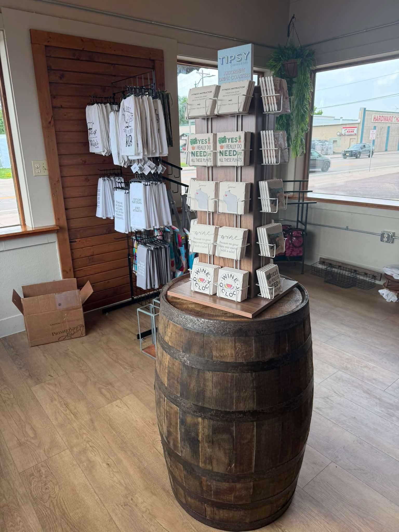 A whiskey-barrel display table in the shop holding drink coasters and small gift items, with a hanging floral basket above