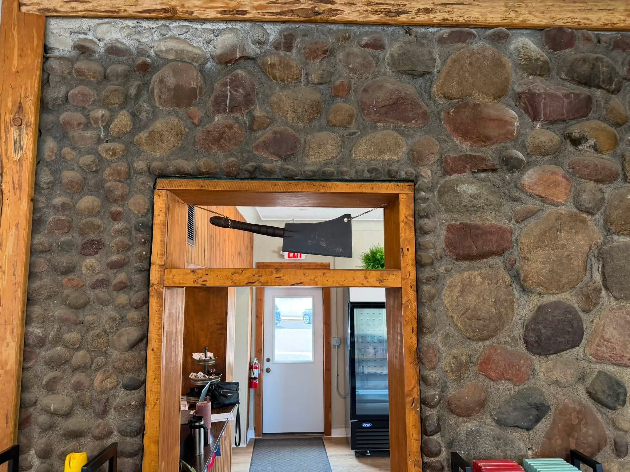 Fieldstone wall framing a wooden doorway with a large decorative meat cleaver suspended above the entry, leading into a back room