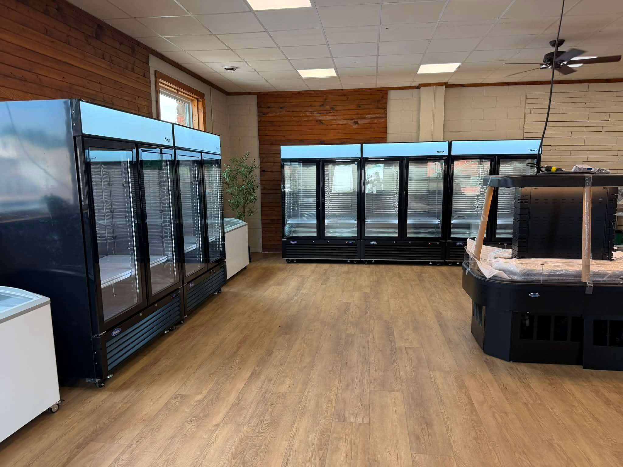 Commercial refrigeration units installed at the shop, including glass-door merchandisers and a curved-glass deli case, ready for stocking