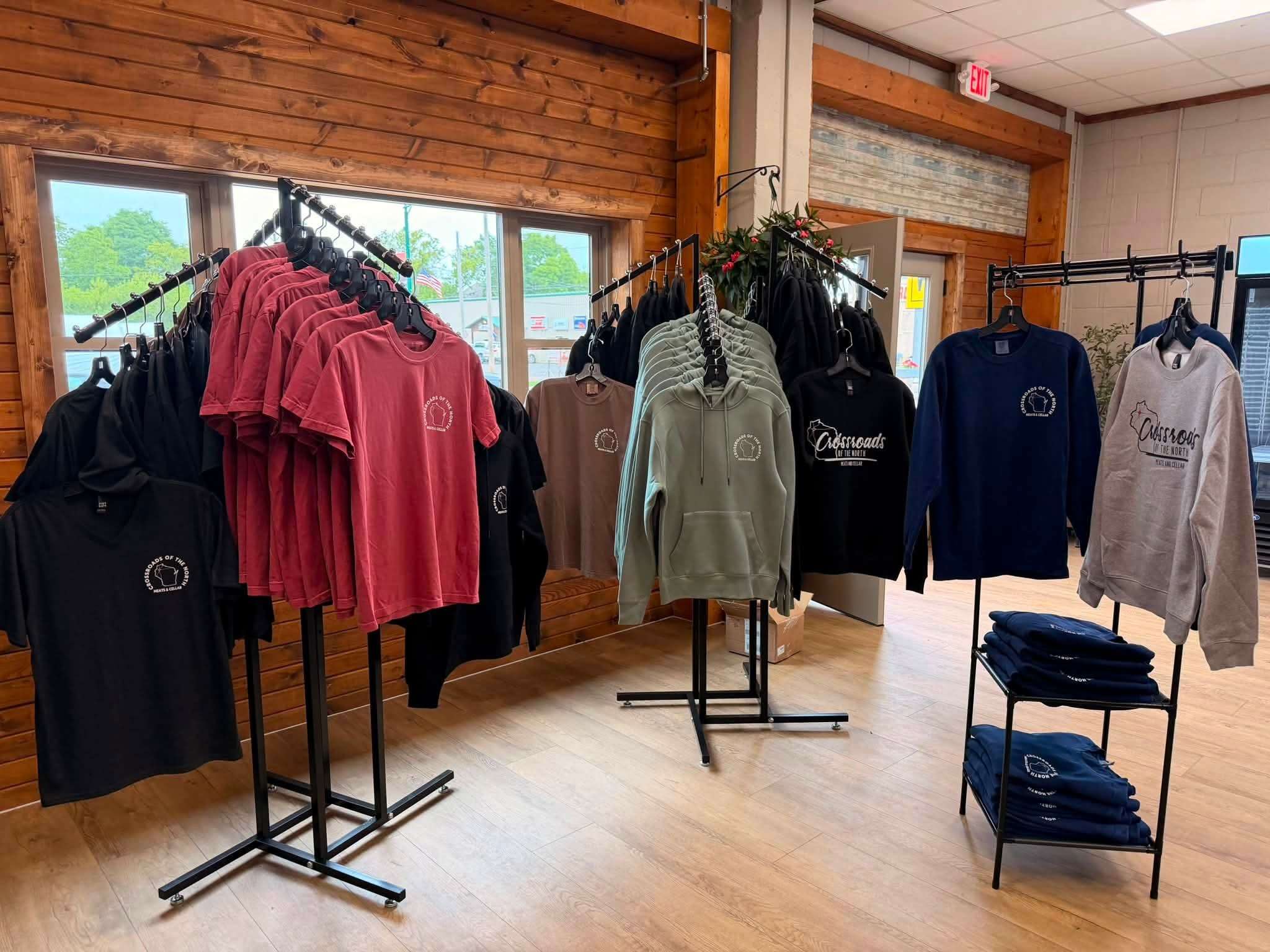 Crossroads of the North branded apparel racks inside the shop, with Wisconsin-logo tees and hoodies on display