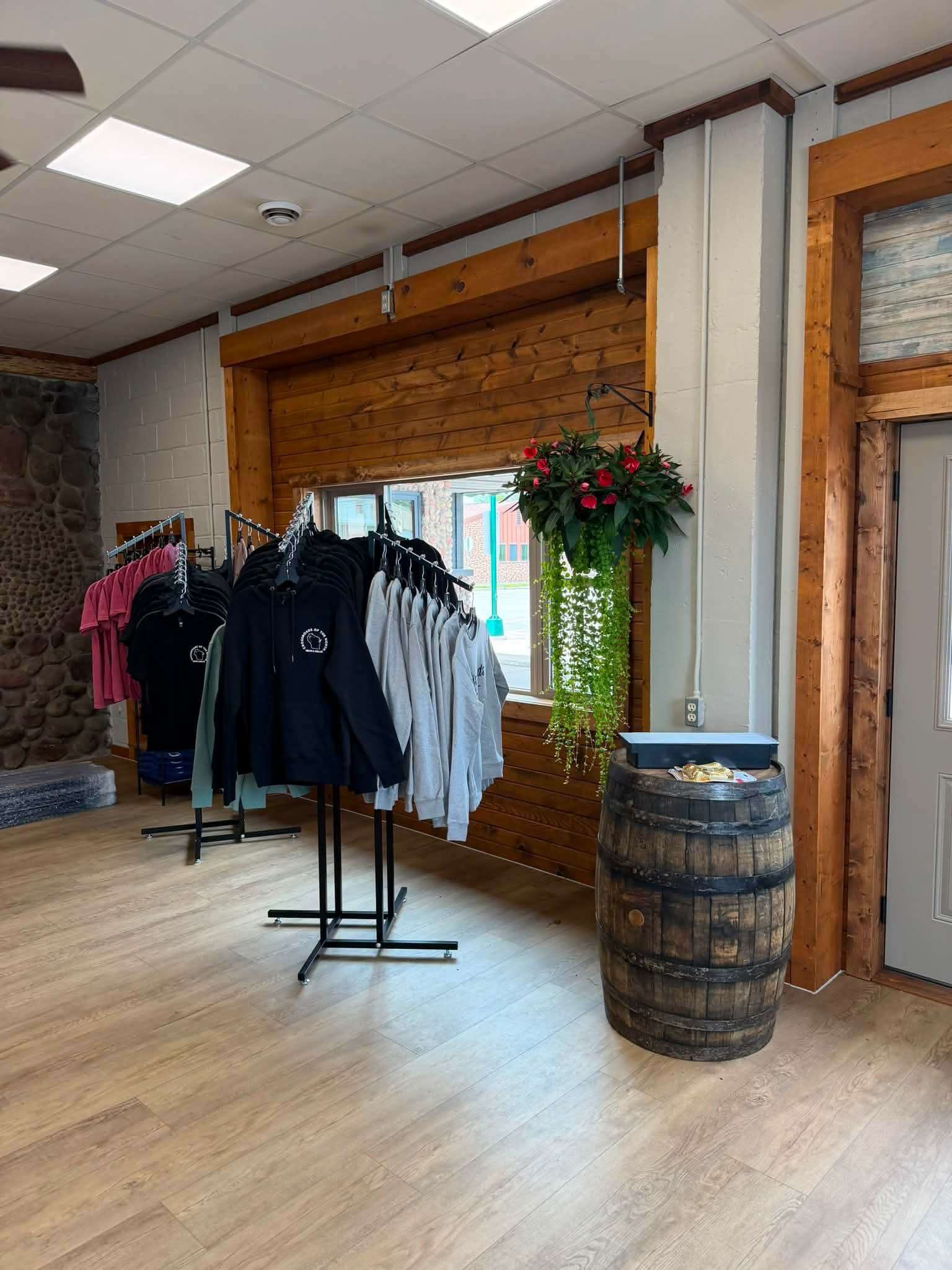 Shop interior with rolling clothing racks, a whiskey-barrel display table, and a hanging floral basket