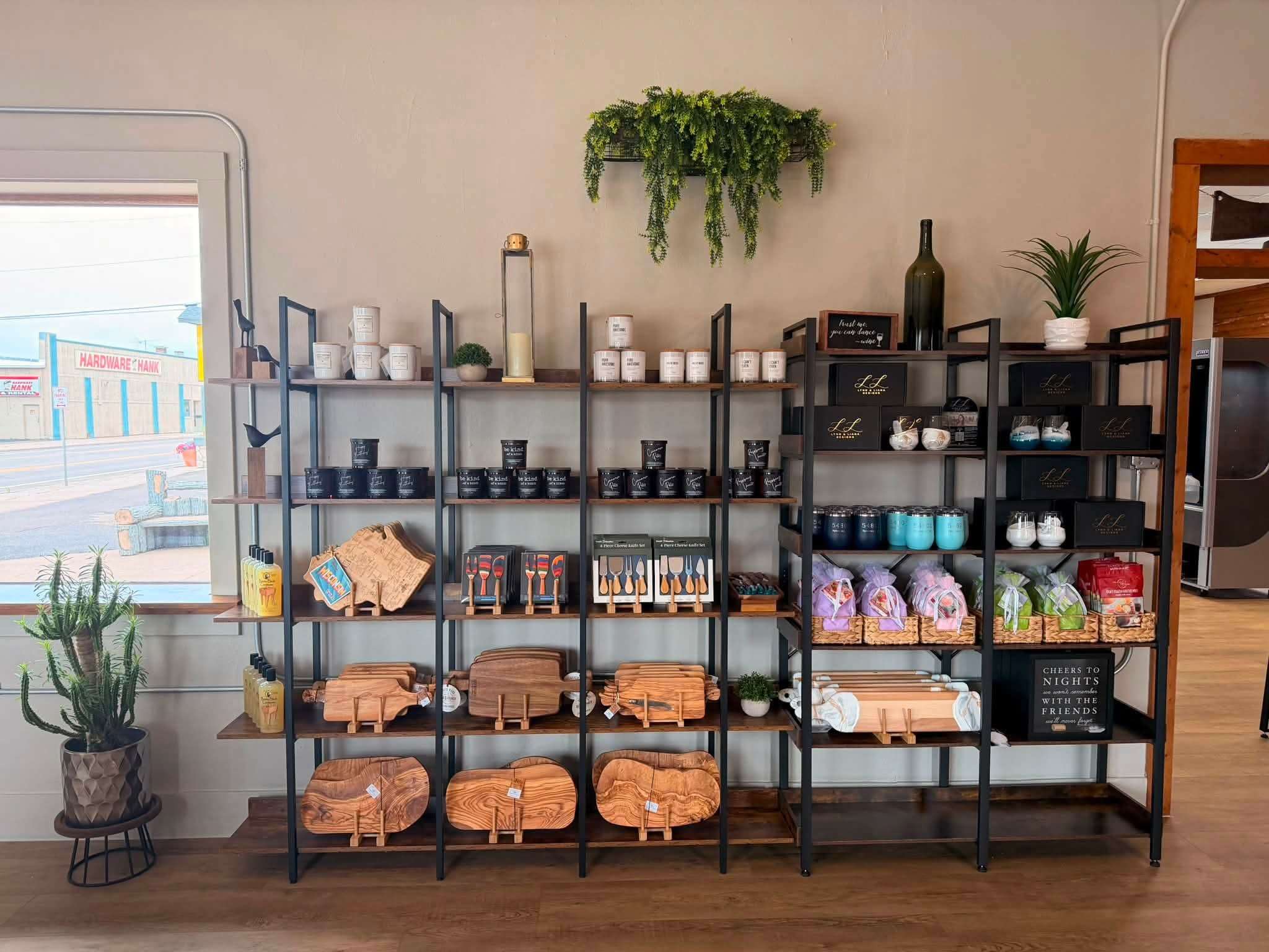 Display shelves with wooden cutting boards, charcuterie boards, kitchen knives, candle tins, and gift baskets