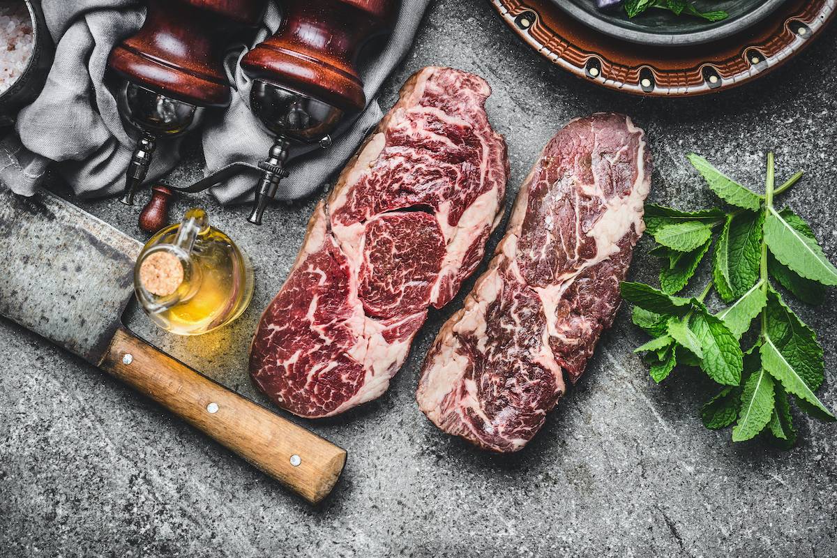 Marbled dry-aged steaks with cleaver, olive oil, and fresh herbs